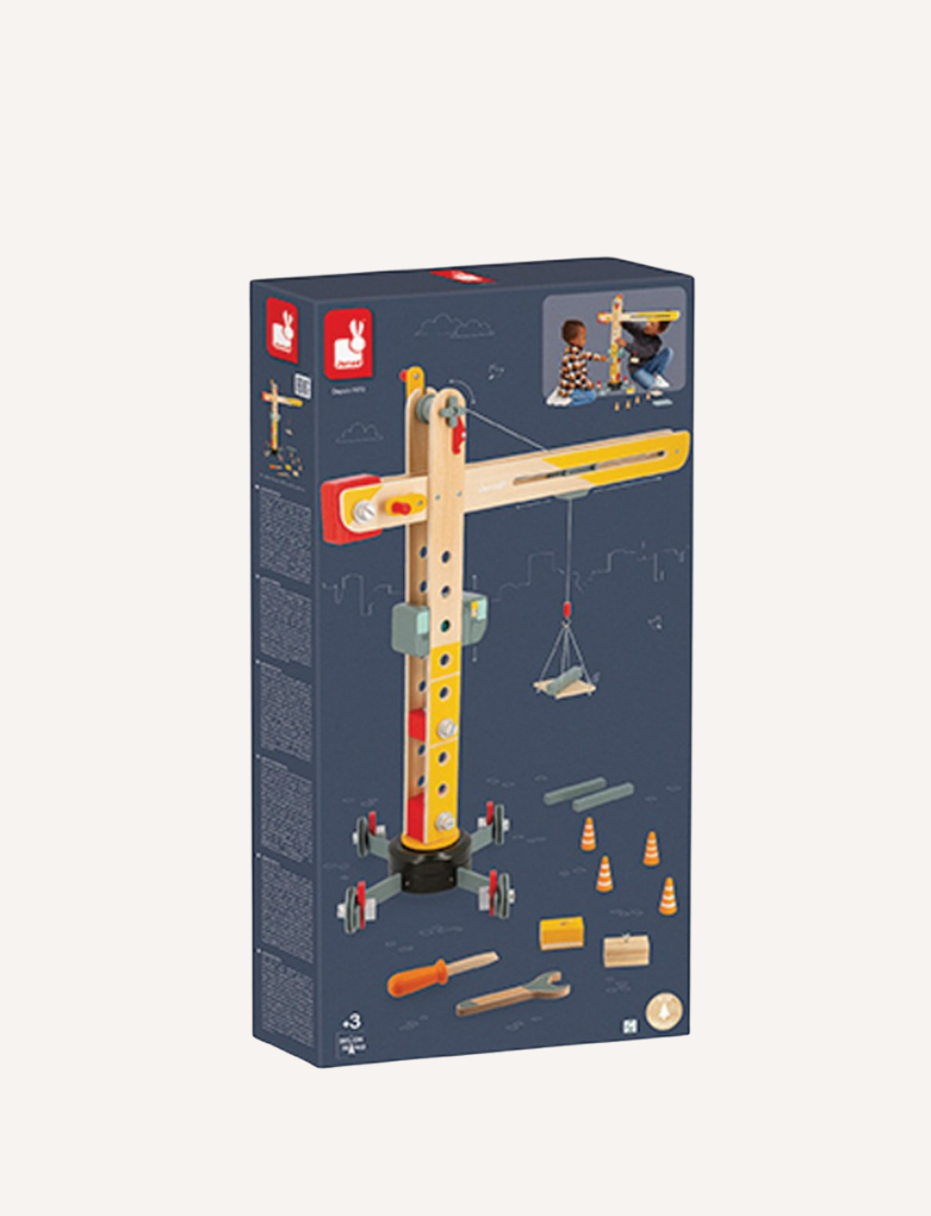 The image features the Janod Giant Crane, a wooden toy that resembles a large construction crane with a base, movable arm, and pulley system. Scattered around its base are various small tools and accessories, including a screwdriver and wrench, making it a delightful role-play toy.