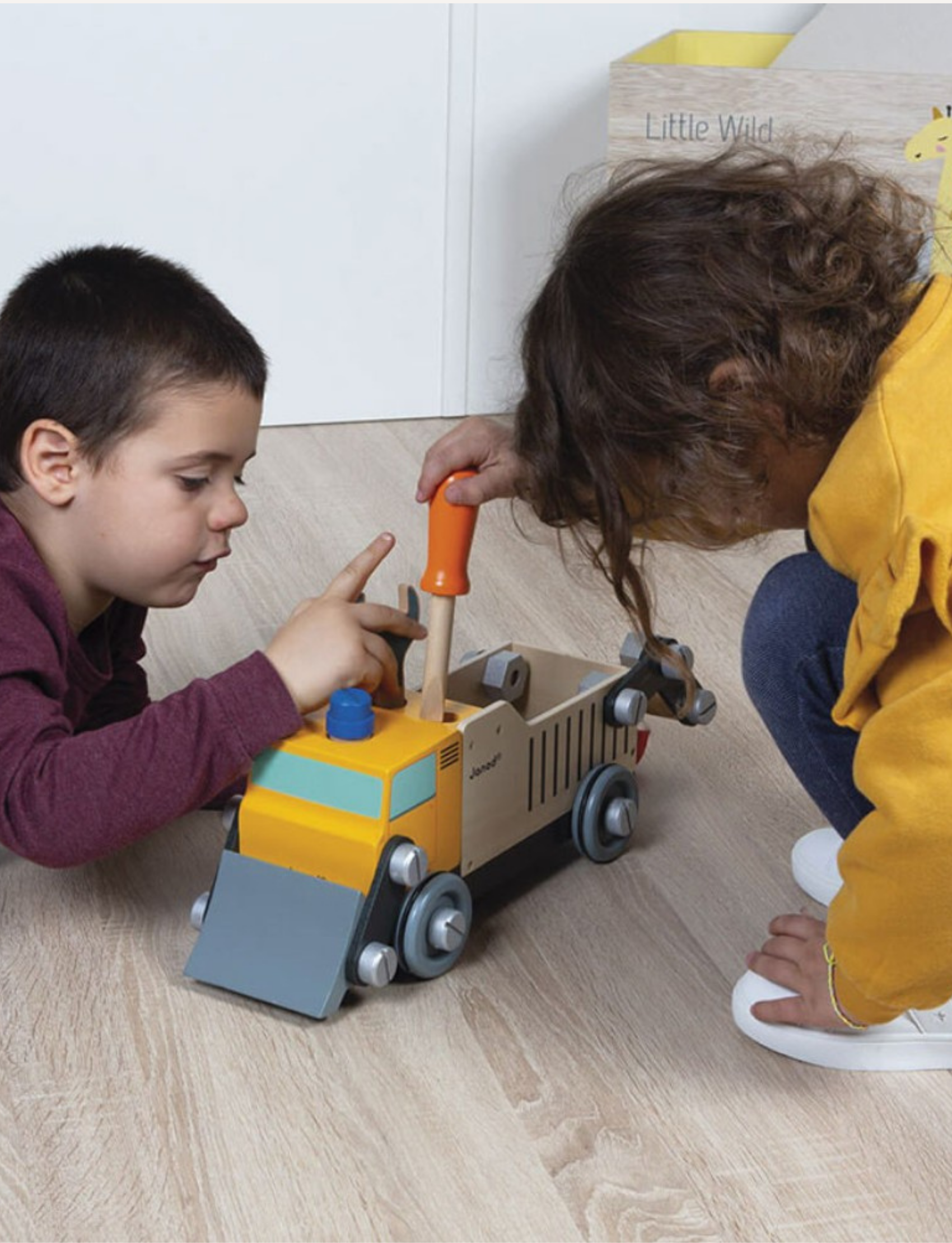 The Janod BricoKids DIY Construction Truck boasts a crane-like movable arm, attached tools, and vibrant red, silver, and blue accents. Made with FSC wood, this yellow and wooden construction truck has a small cabin, wheels, and various mechanical elements crafted from both wood and plastic.