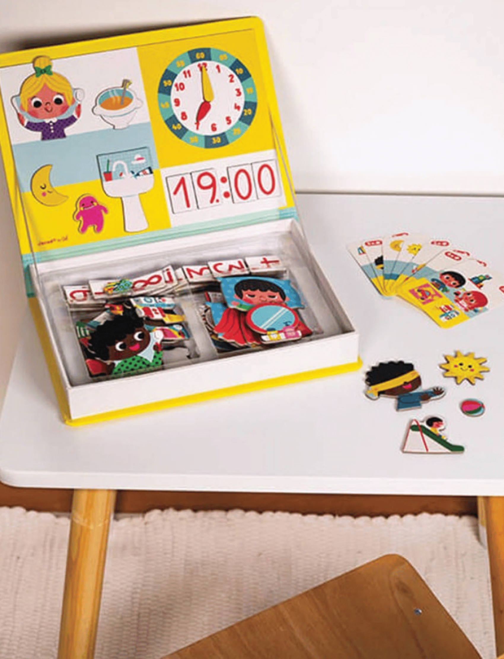 The "Learn Time Magnetic Book" by Janod is a children's educational toy set that includes a vibrant board with cartoon characters, a clock showing 12:15, and various magnetic pieces for storytelling and activity cards. The magnetic book is propped open, displaying all the pieces neatly within the storage area to help kids learn to tell the time.