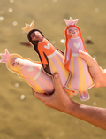 Three vibrant Dive Buddies from Sunnylife float on a swimming pool's surface. The toys feature a yellow and white striped design, a green spiky design, and a blue one with a red mouth. Sunlight gleams off the water, creating ripples and reflections.