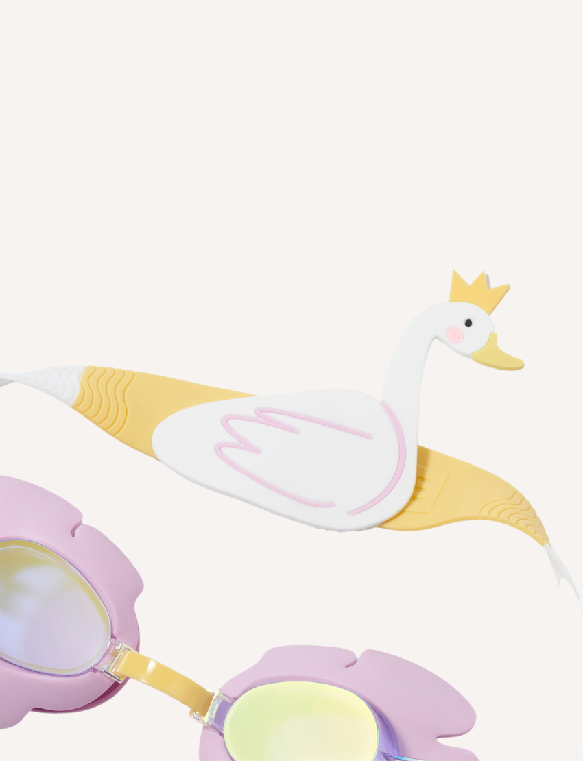 The Kids Swim Goggles by Sunnylife feature a playful swan-shaped head strap, with purple frames and reflective lenses. The head strap showcases a white body and yellow accents, complete with a crown. Both items are displayed against a plain white background.