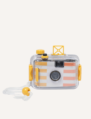 A Sunnylife Underwater Camera, encased in a transparent protective shell with yellow accents, rests on a textured stone surface. The camera boasts a focus-free 28mm lens and features a striped design in white, orange, and yellow.