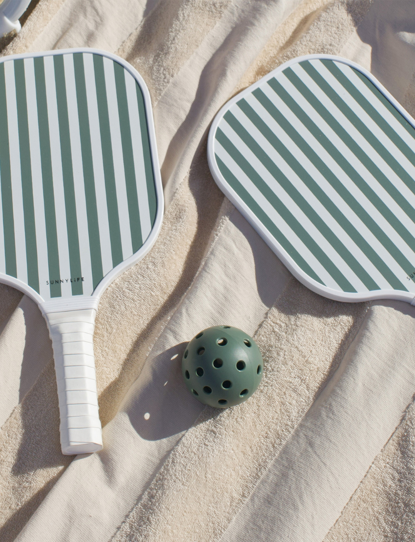 Two paddles from the Sunnylife Pickleball Set, featuring green and white stripes, are placed side by side. A green pickleball with holes is situated nearby on a simple white background.