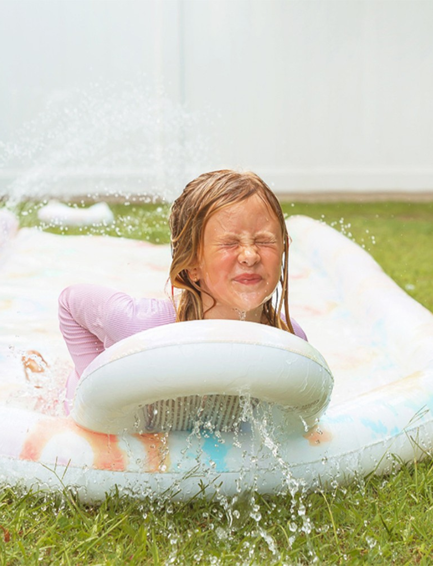 Image of the Sunnylife Slip, Slide and Body Board Set - Tie Dye Multi, showcasing a light pastel tie-dye pattern featuring swirls of pink, blue, and yellow. Two small inflatable pool rings with matching patterns are positioned next to the slide against a plain white background.