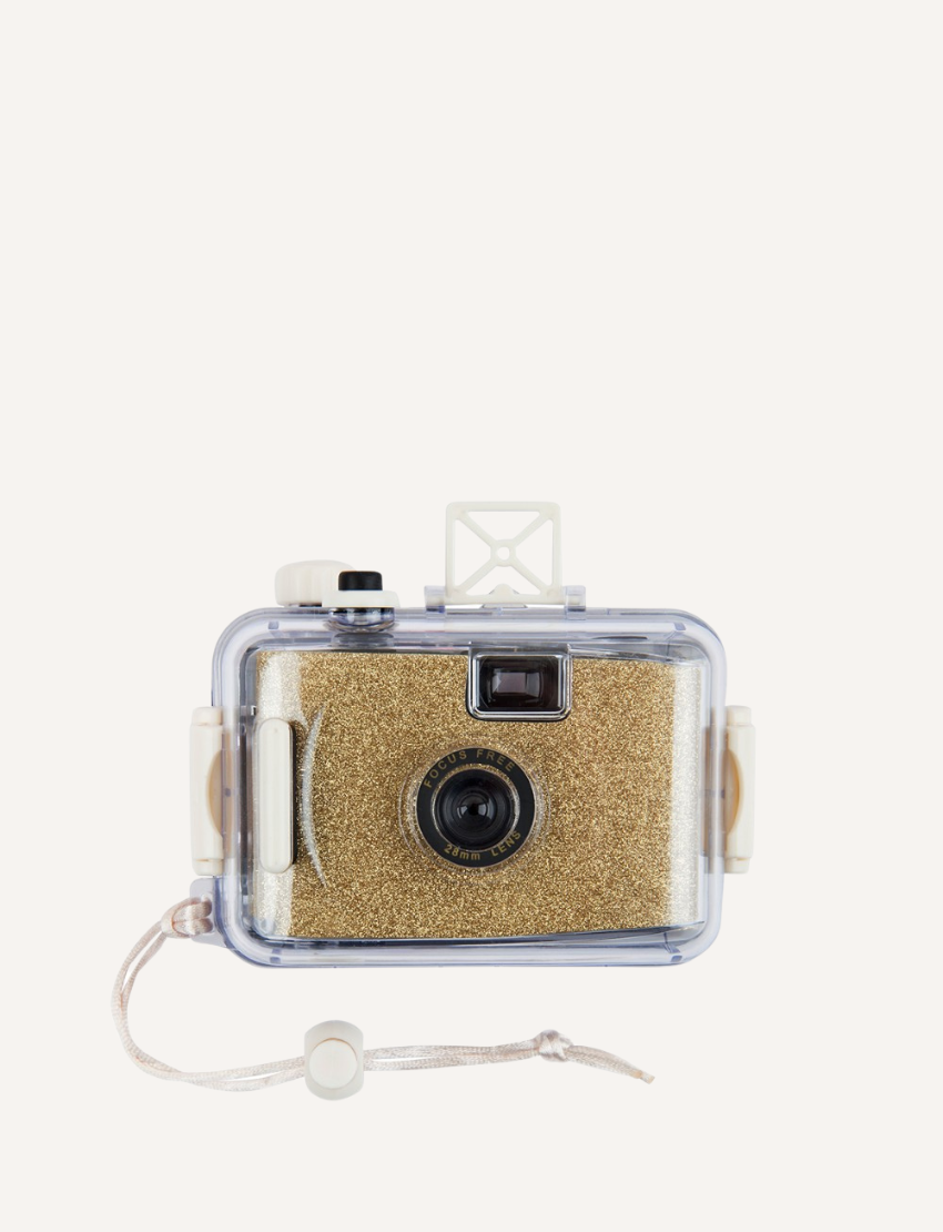 The Sunnylife Underwater Camera - Glitter Gold sits centered against a plain white background, enclosed in a transparent waterproof casing. Featuring buttons and a wrist strap, it suggests suitability for outdoor or underwater use.