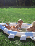 The Kids Sprinkler Mat Into the Wild - Blue by Sunnylife is displayed. This inflatable children's pool, designed in the shape of a chameleon, showcases a blue and white color scheme with intricate details including a tail, legs, and a chameleon head on one side. Currently, the pool is deflated and laid out flat.