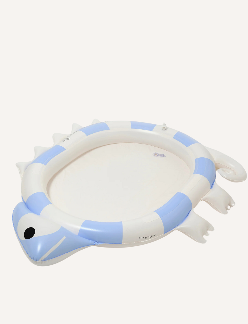 The Kids Sprinkler Mat Into the Wild - Blue by Sunnylife is displayed. This inflatable children's pool, designed in the shape of a chameleon, showcases a blue and white color scheme with intricate details including a tail, legs, and a chameleon head on one side. Currently, the pool is deflated and laid out flat.