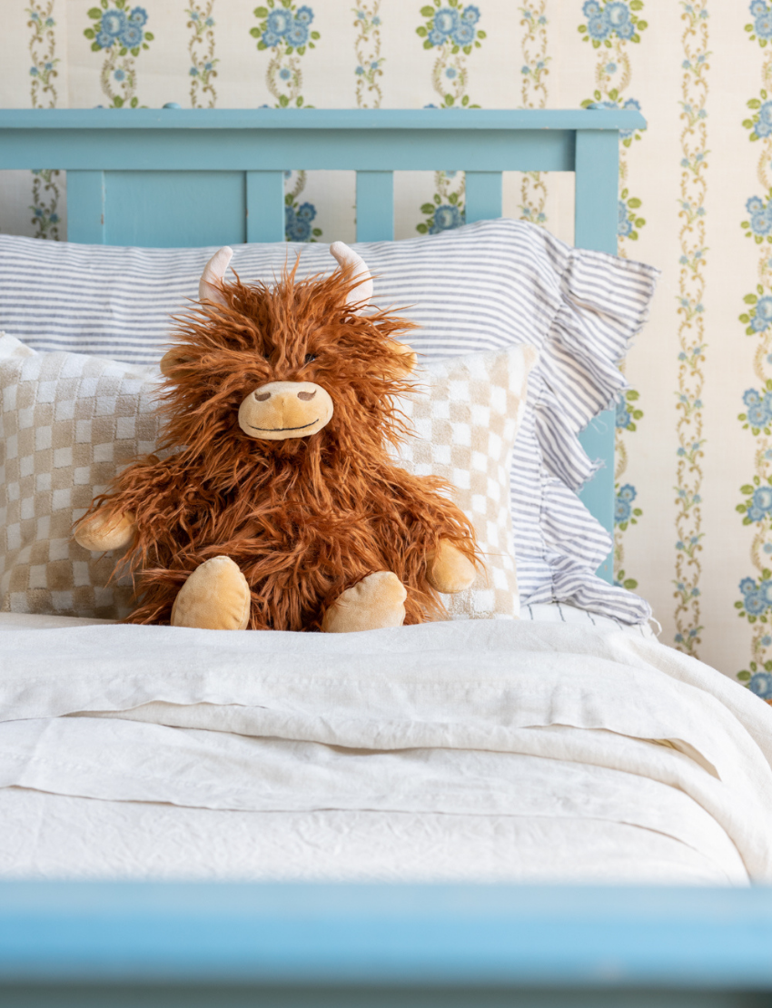 Henry The Highland Cow, by Nana Hutchy, is a soft toy that looks like a shaggy brown highland cow with long hair, beige hooves, horns, and a smiling face. This children's soft toy sits upright against a plain white background and is perfect for cuddles and play.