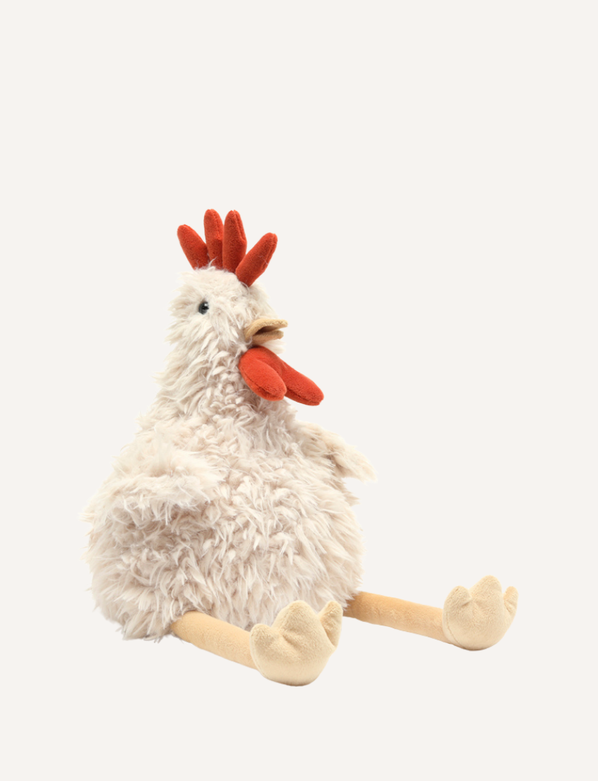 The image showcases Roy the Rooster, a plush toy from the brand Nana Huchy. This adorable chicken-shaped toy features a fluffy white body, red comb and wattle, and beige legs complete with soft feet. Sitting upright against a plain background, this soft and huggable toy is all set for any child's adventure.