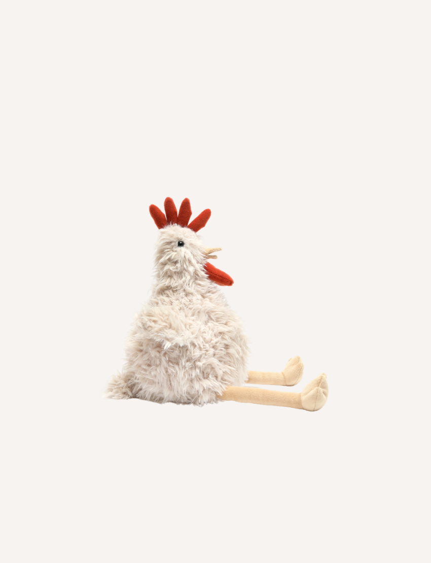 Roy the Rooster, a white and fluffy stuffed animal by Nana Hutchy, resembles a chicken with an orange comb, wattle, and beak. It has beige legs and feet and is sitting upright against a plain background.