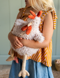 Roy the Rooster, a white and fluffy stuffed animal by Nana Hutchy, resembles a chicken with an orange comb, wattle, and beak. It has beige legs and feet and is sitting upright against a plain background.