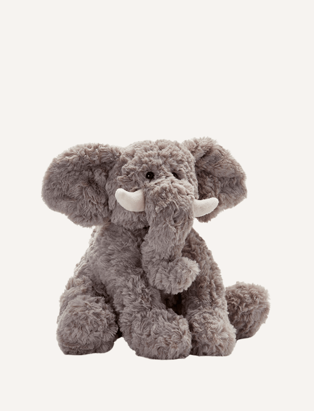 Jimmy the Elephant from Nana Hutchy is pictured against a plain white background. This plush gray elephant toy features a soft body, endearing large floppy ears, a long trunk, and white tusks. Sitting with its trunk slightly curled, this adorable toy captures hearts effortlessly.