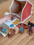 Introducing the Fabric House - Little Farm by Fabelab: a charming toy set made from organic cotton. This delightful children’s playhouse barn features an open front and comes with small plush animals and figures, including a horse, chicken, person, and sheep. The barn is adorned with farm-themed illustrations that spark imaginative play and includes a convenient handle for easy carrying.