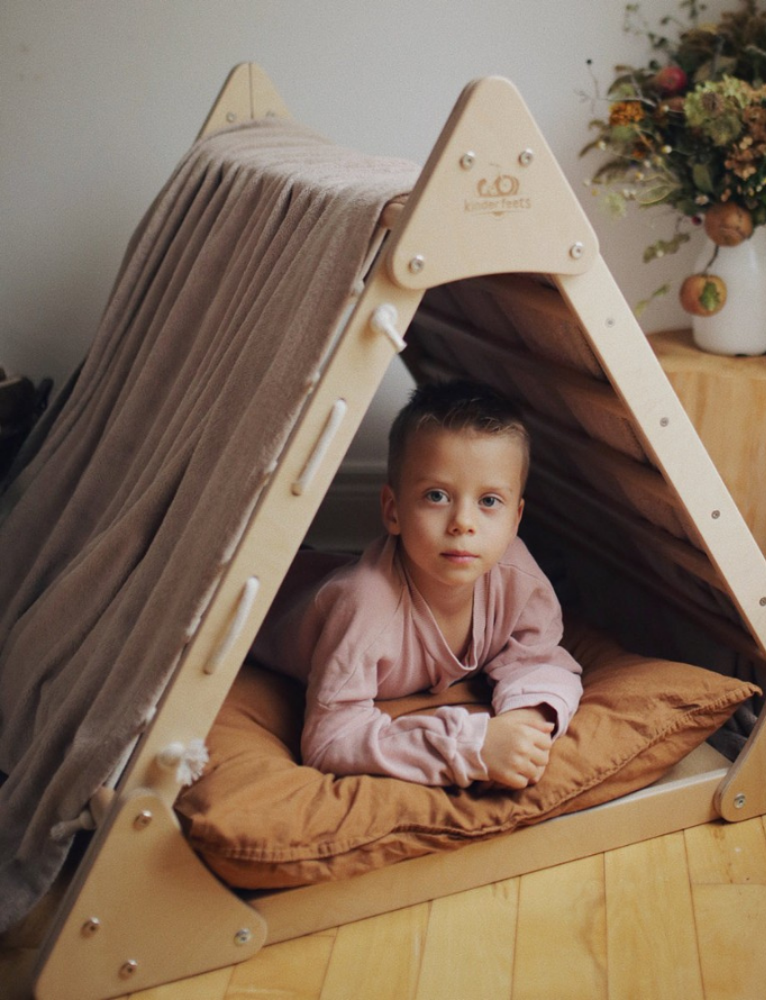 The Artiwood Pikler Slide and Climber Set is a wooden climbing structure for children featuring an A-frame design. One side has horizontal climbing steps, while the other side incorporates a net for climbing. The wood is lightly finished to accentuate its natural grain.