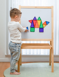 The Connetix Tiles Rainbow Mini Pack 24-Piece set is on display. The packaging features a purple and beige design with illustrations of vibrant magnetic tiles creating a rocket and various shapes. It includes 24 pieces and is suitable for children aged 3 and older.