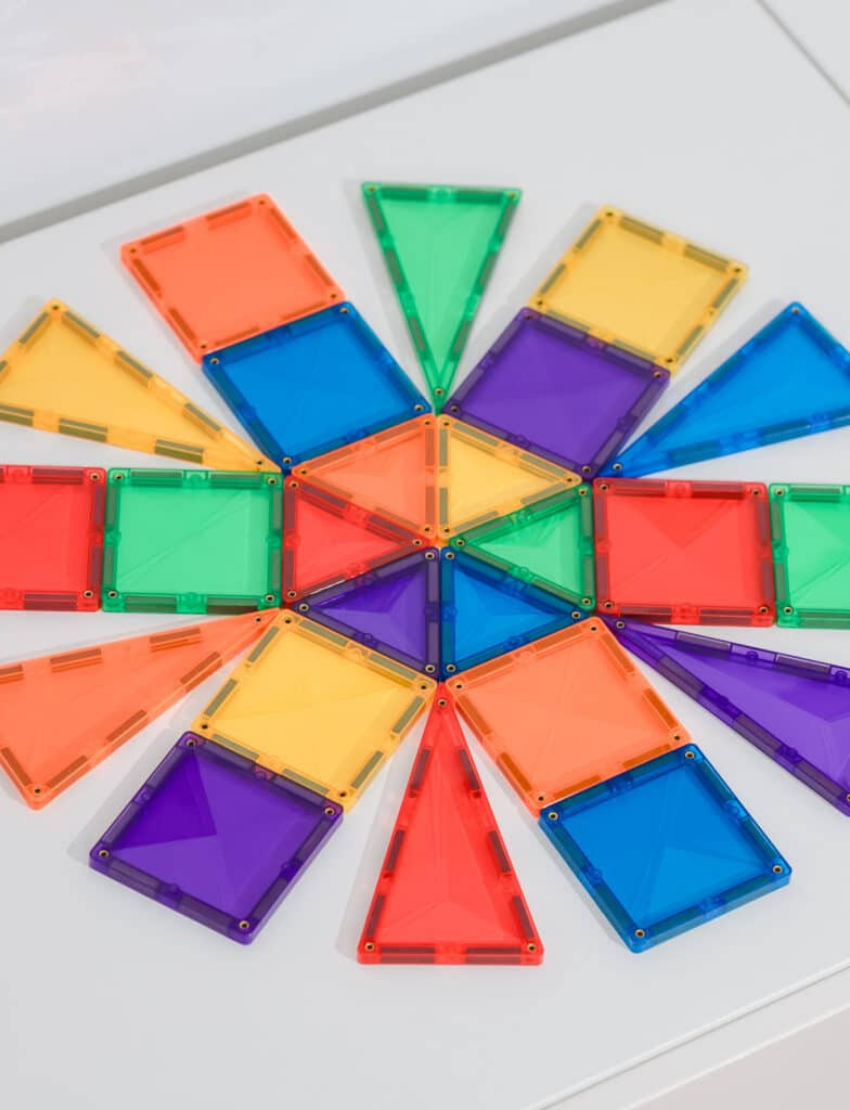 The Connetix Tiles Rainbow Mini Pack 24-Piece set is on display. The packaging features a purple and beige design with illustrations of vibrant magnetic tiles creating a rocket and various shapes. It includes 24 pieces and is suitable for children aged 3 and older.