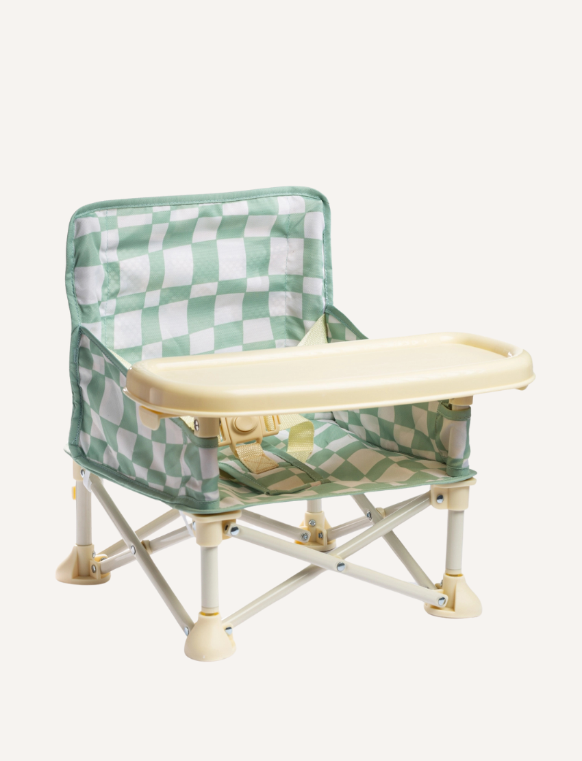 A pink and white checkered portable IZIMINI Baby Chair with a tray is set against a plain background. The lightweight, collapsible frame ensures easy transportation, making the high-chair adaptable for any outing or mealtime adventure.