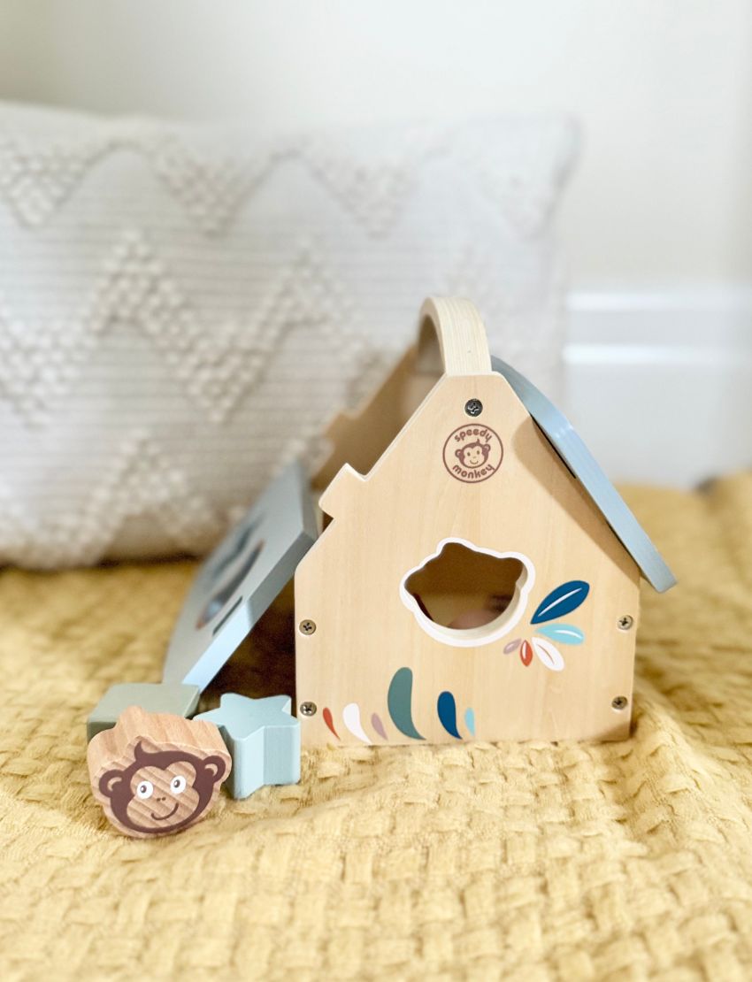 The Speedy Monkey House Shape Sorter with 8 blocks is a charming wooden toy, designed as a house and made from sustainably sourced wood. It includes vibrant geometric blocks such as stars, circles, and squares. The house features a blue roof with cut-out shapes and a convenient carry handle, ensuring both enjoyable and eco-friendly playtime for early learners.