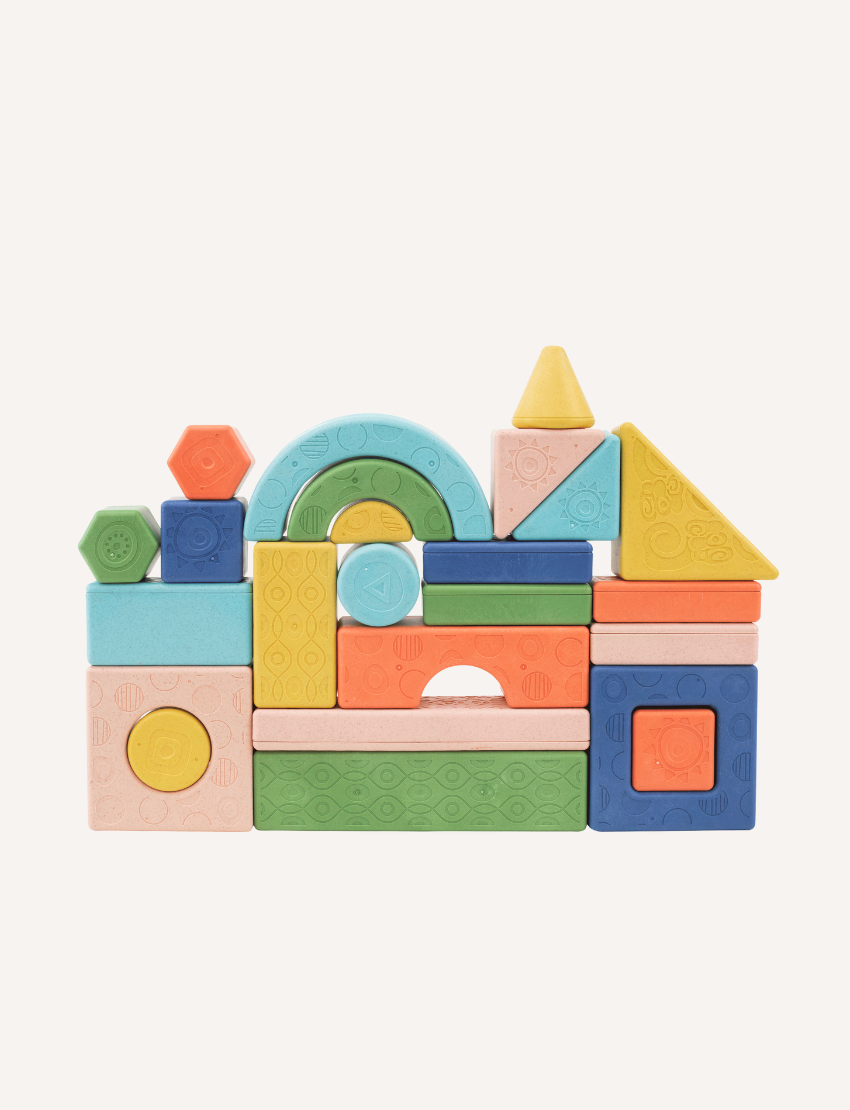 The "Rattle & Stack Blocks - Deluxe Pack of 24" from Tiger Tribe includes a vibrant collection of blocks in different shapes and sizes. The packaging is eco-friendly, designed for children aged 1-4, and features a convenient handle for easy transportation.