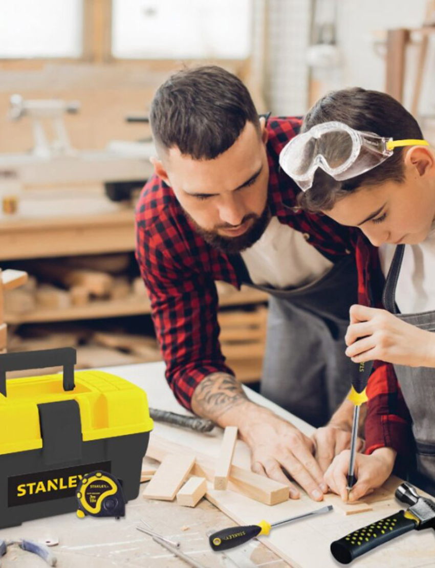 A toolbox featuring a yellow and black design labeled "Stanley" comes with a 5-piece tool set consisting of a hammer, screwdriver, measuring tape, and safety goggles. The tools feature black handles accented with yellow.