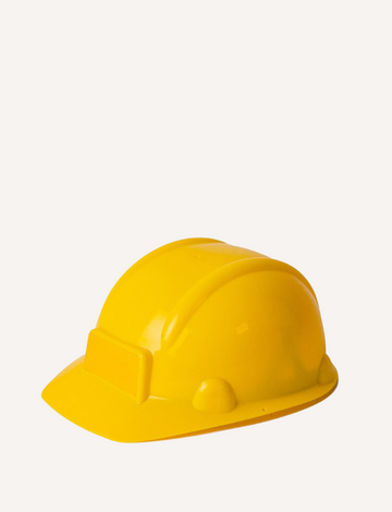 A child, dreaming of becoming a builder, wears a Stanley Construction Helmet and a light blue polo shirt, their face alight with happiness. The out-of-focus backdrop suggests an outdoor environment with dirt, sparking visions of upcoming construction adventures.