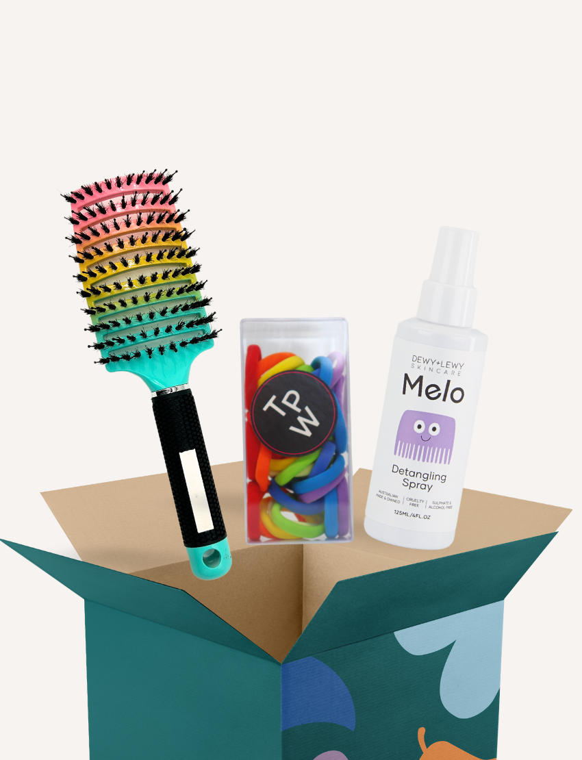 The Melo x SPA Detangle Kit by The Play Way features an open cardboard box with vibrant abstract designs, housing a rainbow-colored hairbrush, a container of blue and white Play Surf Hair Elastics, and a bottle of Dewy Lewy Melo Detangling Spray. This sensory-friendly kit provides everything you need for seamless hair care.