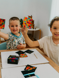 A cardboard box from The Play Way's Mindset Kit contains a package of Liquid Chalks, a pack of Sensory Play Affirmation Cards, and a set of Scratch Rainbow Notes. The Affirmation Cards' package is prominently displayed, with the message reading, 