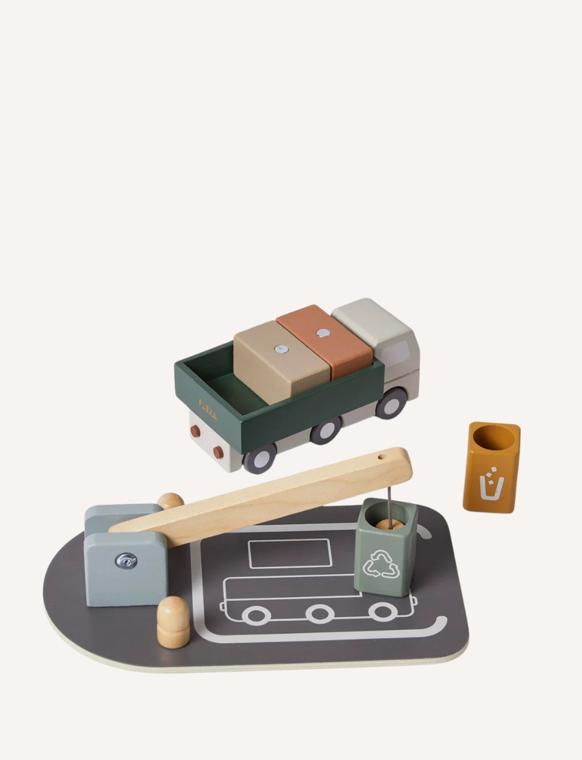 The Flexa Wooden Truck and Crane set includes a truck with block cargo, a balance scale, and two bins marked with recycling symbols. The set features a gray base designed with road patterns and comes with a wooden lever arm. It showcases muted tones of green, brown, and gray.