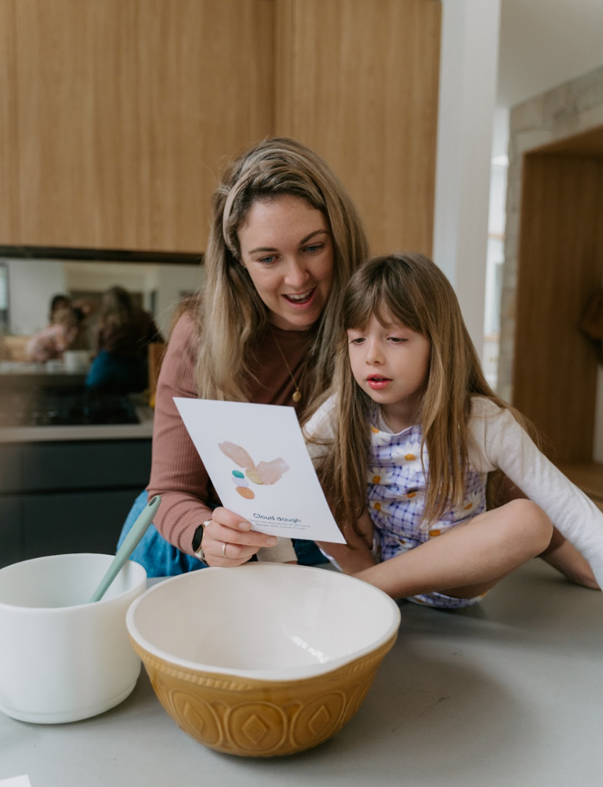 A person holds a Sensory Play Australia card from the "Sensory Play Cards Set in Box" featuring a recipe for "Cloud Dough" and an image of hands holding colorful dough balls. The table also has a whisk, spatula, mixing bowl, measuring cups, and another card from the same set in the background.