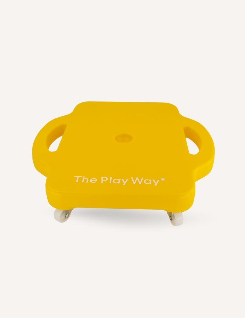 The Play Way's Regulation Through Movement Kit is opened, showcasing a hammock swing with a blue edge, a gray exercise ball, and a yellow scooter board with four casters. Various accessories for sensory regulation can be seen partly inside and around the green and blue box.