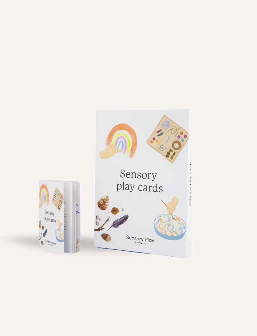 A person holds a Sensory Play Australia card from the "Sensory Play Cards Set in Box" featuring a recipe for "Cloud Dough" and an image of hands holding colorful dough balls. The table also has a whisk, spatula, mixing bowl, measuring cups, and another card from the same set in the background.