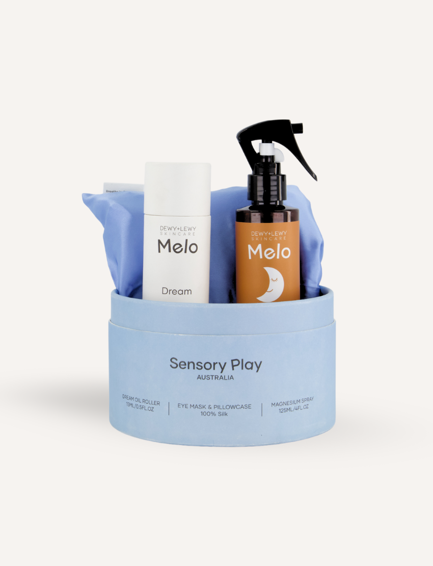 A round, light blue box labeled "Sensory Play Australia" contains the "Sleep Set," which includes a white cylindrical bottle labeled "Melo Dream," a brown spray bottle labeled "Melo," and a folded light blue fabric item, possibly an eye mask or pillowcase.