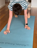 A rolled-up large turquoise yoga mat from The Play Way brand, secured with black straps. The text 