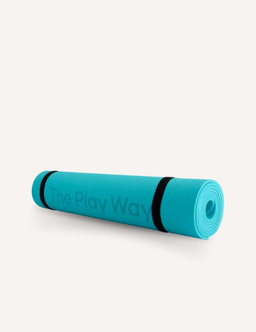 A rolled-up large turquoise yoga mat from The Play Way brand, secured with black straps. The text "The Play Way" is visible on the mat against a plain white background.