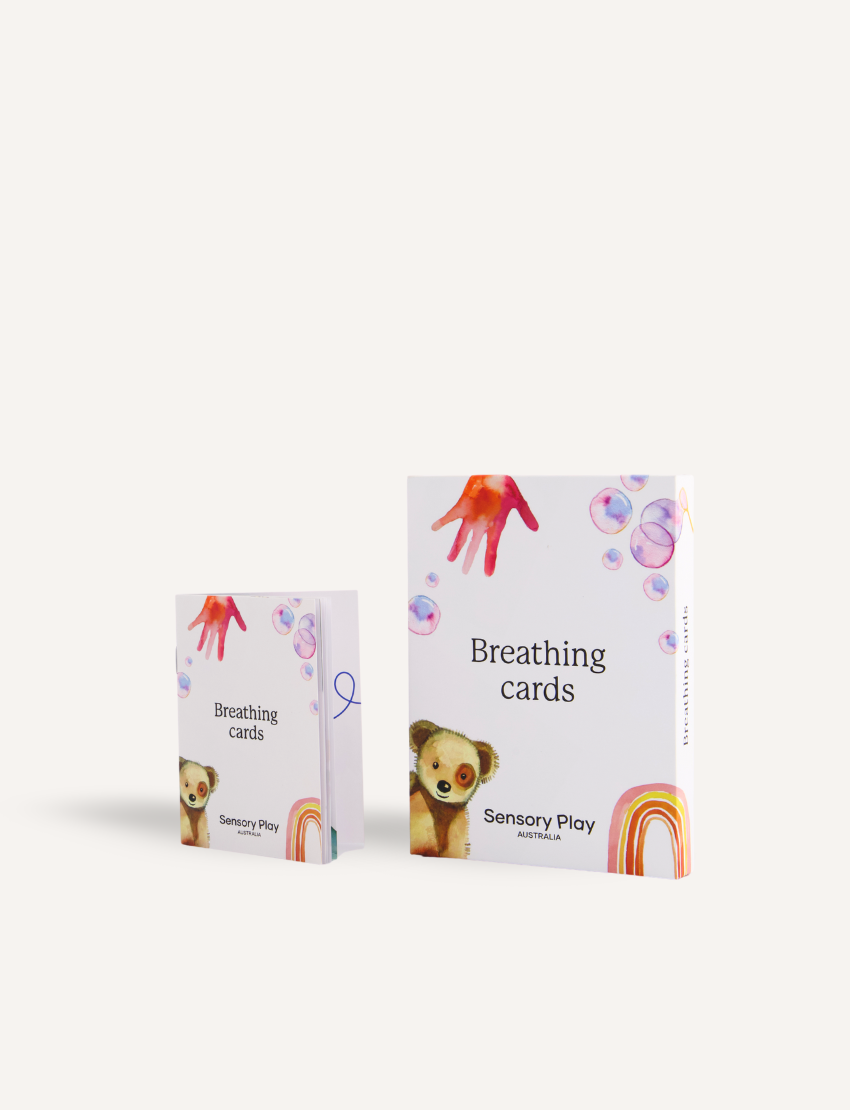 Two boxes of the "Breathing Card Set" by Sensory Play Australia are displayed, intended to improve mindful breathing and self-regulation skills. The larger box features charming illustrations of a teddy bear, rainbow, bubbles, and a hand, while the smaller box mirrors these delightful designs.