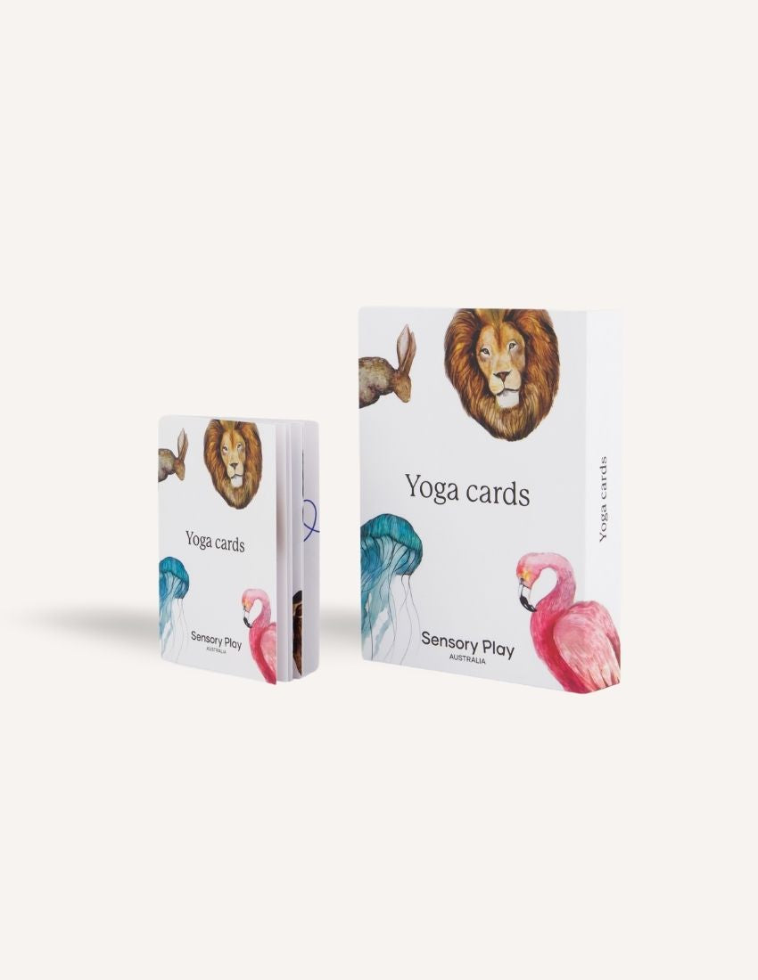 Two sets of the Yoga Card Set by Sensory Play Australia are showcased, encouraging mindfulness in children. The larger set is propped up against the smaller one, and both sets are adorned with artistic illustrations of a lion, rabbit, jellyfish, and flamingo. The packaging prominently displays the product name "Yoga Card Set" along with the brand "Sensory Play Australia.