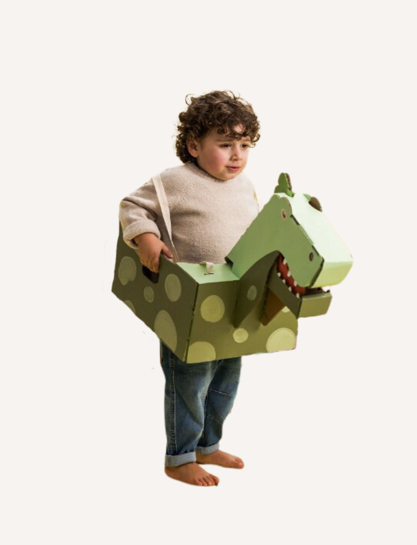 Two children are playing with cardboard animal costumes. The girl on the left is wearing a costume designed like a pink unicorn, and the boy on the right is in Les Petite Artistes' Mean Dinosaur Costume. Both are smiling and engaged in their imaginative role play, showcasing their creative fierceness.