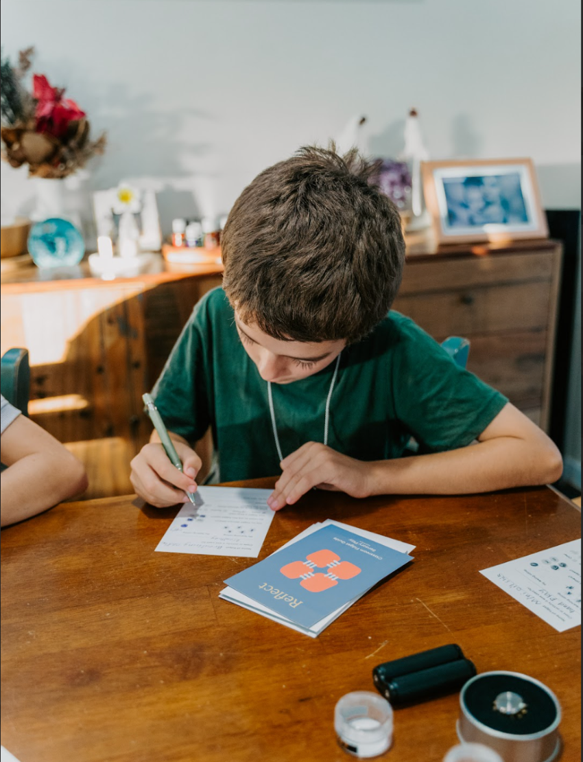 A blue card titled "Reflection Card Set - Attention & Learning" from Sensory Play Australia, featuring an orange interlocking squares design, is displayed in front of an informational brochure outlining the benefits, including self-awareness and emotional regulation, as well as usage instructions for the card set.