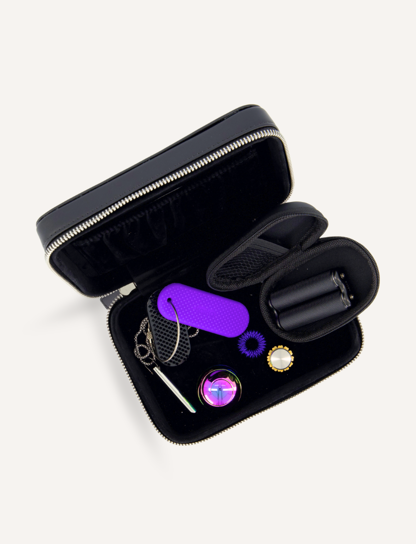 A compact black zippered case, included in the Kaiko Regulation Fidgets Bundle from Kaiko, holds an assortment of accessories designed for sensory regulation and tension relief. The contents are organized neatly and include a purple silicone tag, keychain hooks, a purple ring, a black cylindrical item, and a patterned button.