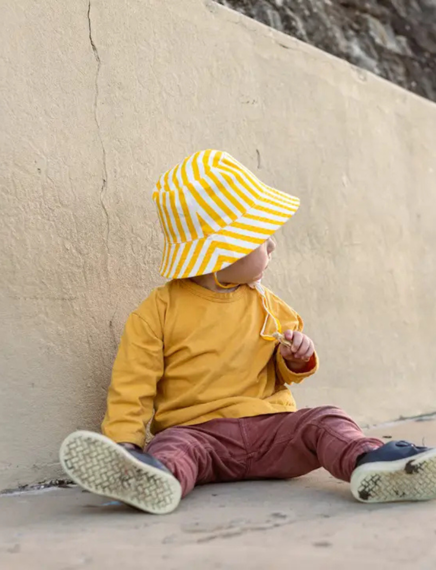 The IZIMINI Cotton Baby Hat is a vibrant bucket hat with a floral print of pink, orange, blue, and green leaves on white. Perfect for outdoor adventures with its wide brim and rounded top, it offers stylish sun protection.