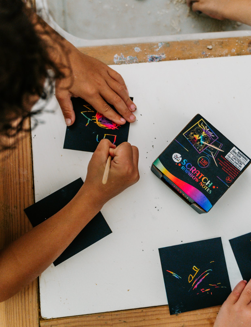 A box labeled "Scratch Rainbow Notes" by Jar Melo features an image of a vibrant scratch art owl. The packaging includes a warning about small parts, suggesting it is suitable for ages 3 and up, and the bottom showcases a colorful rainbow gradient design.