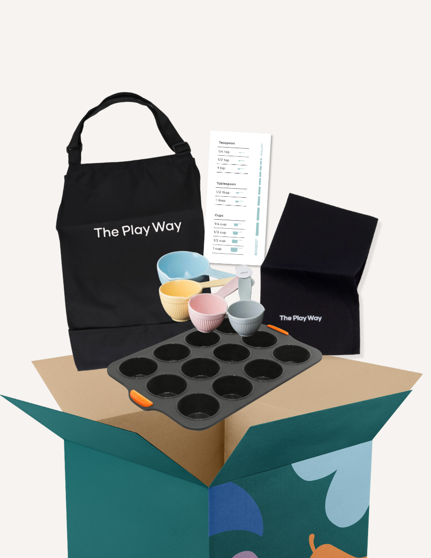 The Play Way's "Getting Started with Baking Kit" unpackaged, showcasing an apron, muffin tin, measuring bowls, and recipe card.