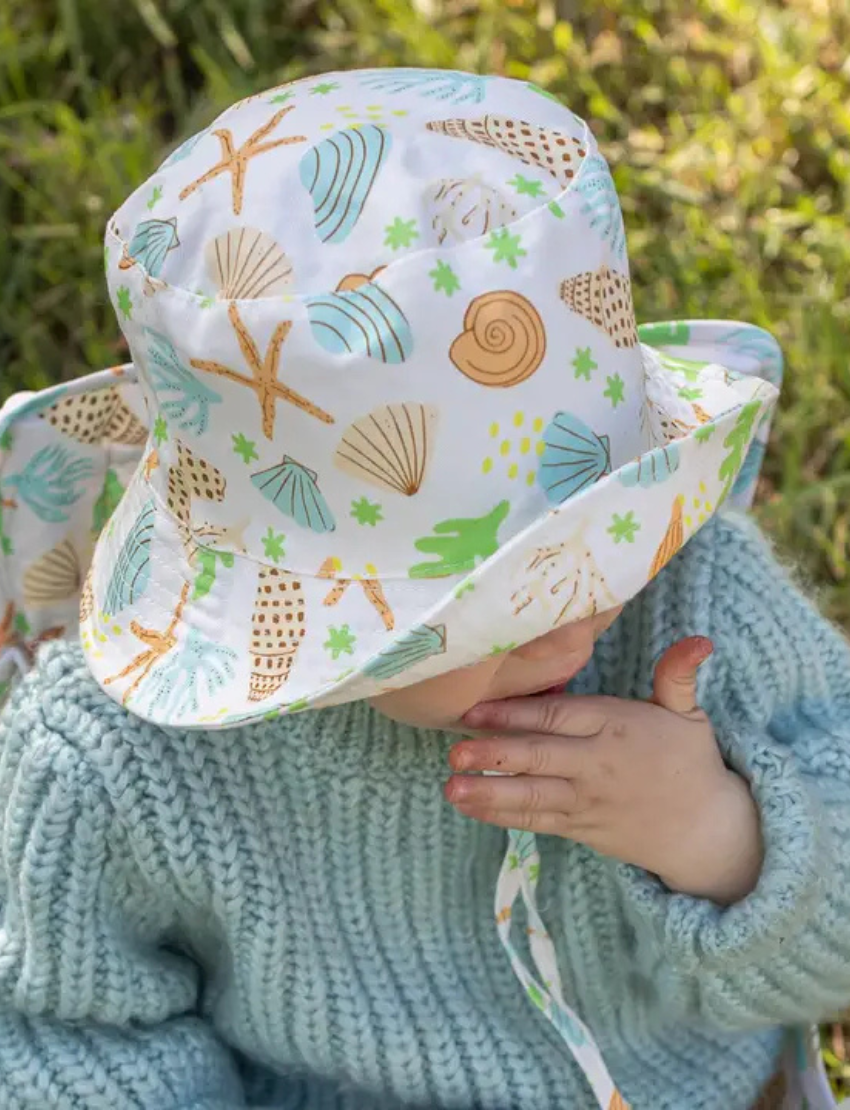 The IZIMINI Cotton Baby Hat is a vibrant bucket hat with a floral print of pink, orange, blue, and green leaves on white. Perfect for outdoor adventures with its wide brim and rounded top, it offers stylish sun protection.