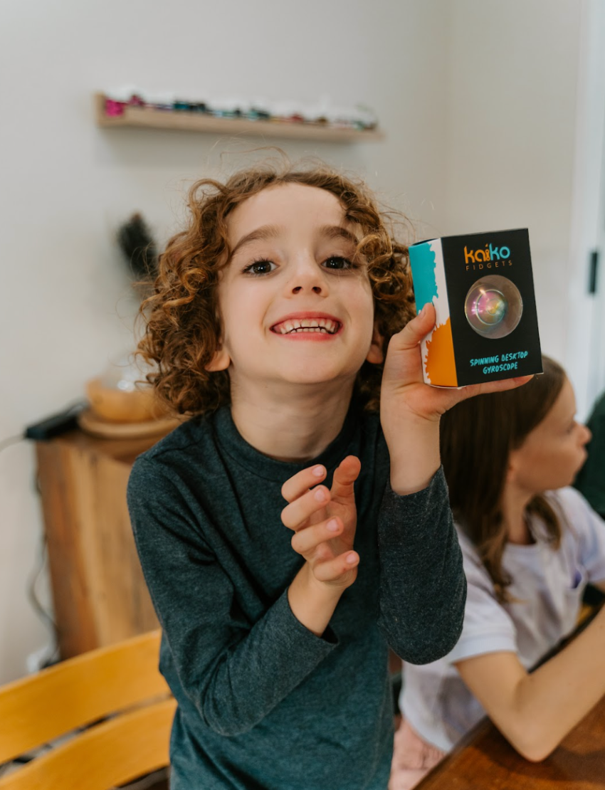 The Kaiko Regulation Fidgets Bundle by The Play Way comes in a black zippered carrying case that opens to reveal various items inside, including a purple silicone fidget, a metallic tool, a keychain, and other small accessories. Ideal for sensory regulation, the interior features a black velvety lining and mesh compartments for organization.