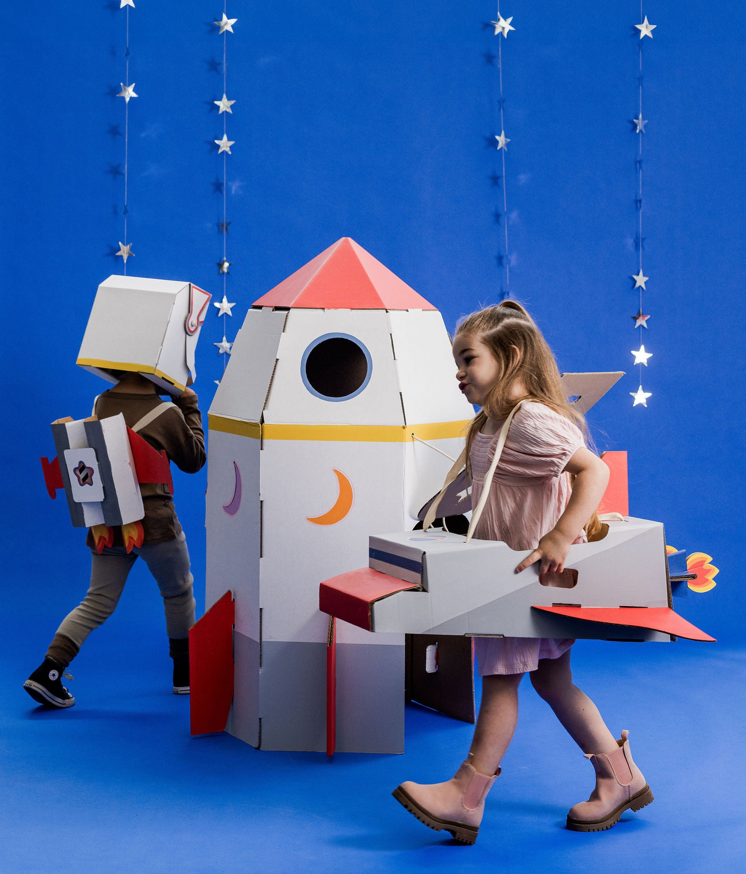 Kids in space costumes with a cardboard rocket and spaceship prop