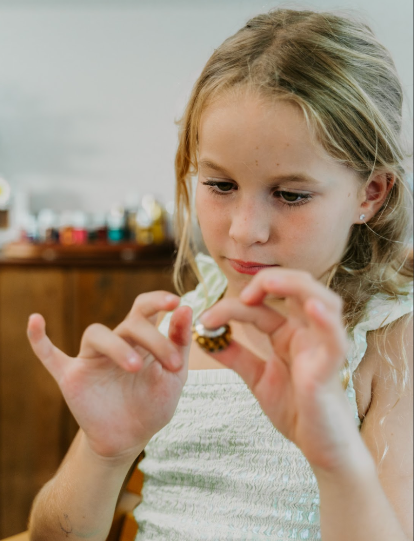 The Kaiko Regulation Fidgets Bundle by The Play Way comes in a black zippered carrying case that opens to reveal various items inside, including a purple silicone fidget, a metallic tool, a keychain, and other small accessories. Ideal for sensory regulation, the interior features a black velvety lining and mesh compartments for organization.