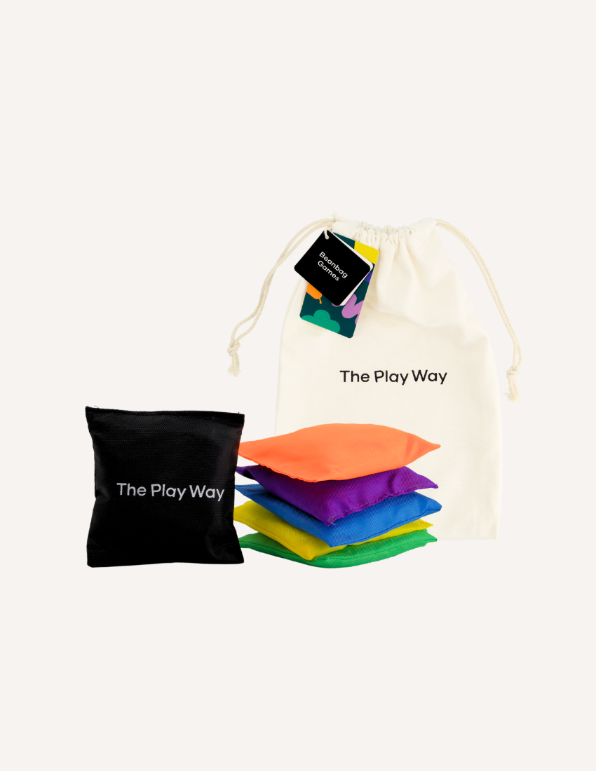 A beige drawstring bag labeled "Bean Bags and Ways to Play Booklet" from The Play Way brand sits beside a stack of colorful bean bags in orange, purple, green, blue, and yellow. A black bean bag with the same label completes the set. The small tag reads "The Play Way: An Indoor/Outdoor Fun Game," perfect for honing fine and gross motor skills.