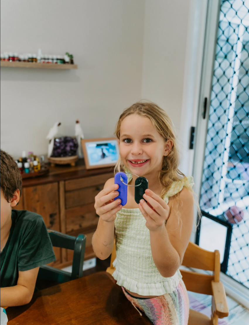 The Kaiko Regulation Fidgets Bundle by The Play Way comes in a black zippered carrying case that opens to reveal various items inside, including a purple silicone fidget, a metallic tool, a keychain, and other small accessories. Ideal for sensory regulation, the interior features a black velvety lining and mesh compartments for organization.