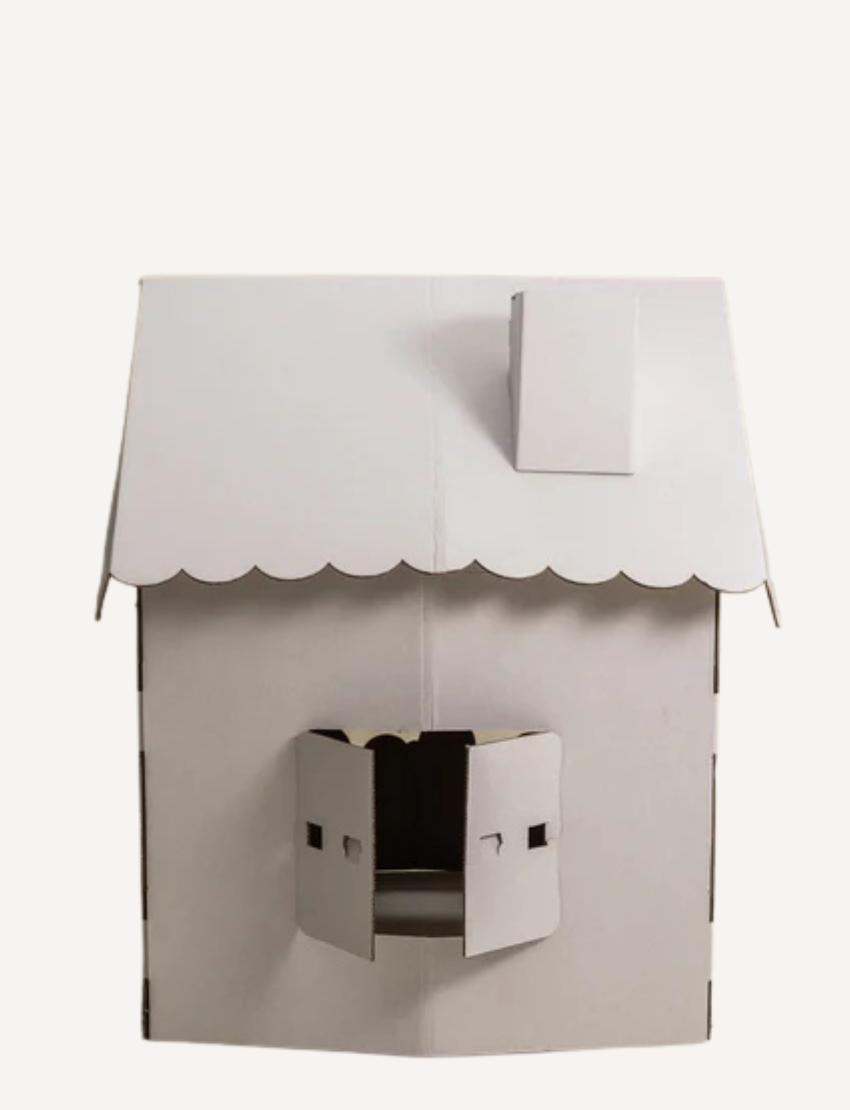 The Scalloped Cardboard House by Les Petite Artistes is a small white playhouse with a pitched roof and chimney. It features an open front with two window shutters and maintains a minimalist design, characterized by clean lines and a plain surface.