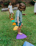 A stack of colorful Stepping Stones from Sensory Play Australia is displayed, perfect for children to develop their gross motor skills. The top stone features a green design with an embossed foot, followed by purple, red, blue, and yellow stones in descending order. These stones are ideal for children's play or physical activities.